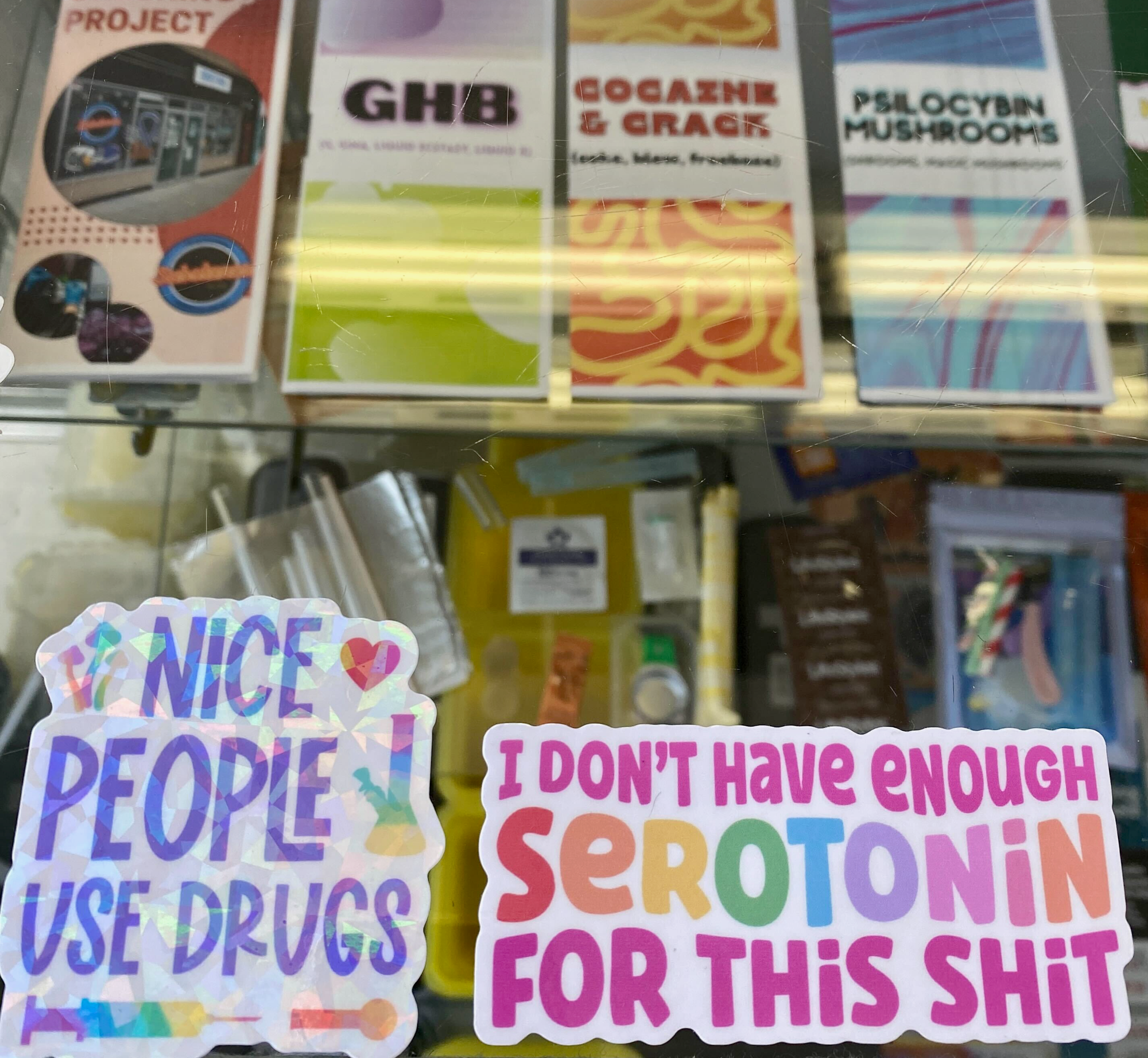 Image features a display case with harm reduction pamphlets, safer consumption supplies, and stickers